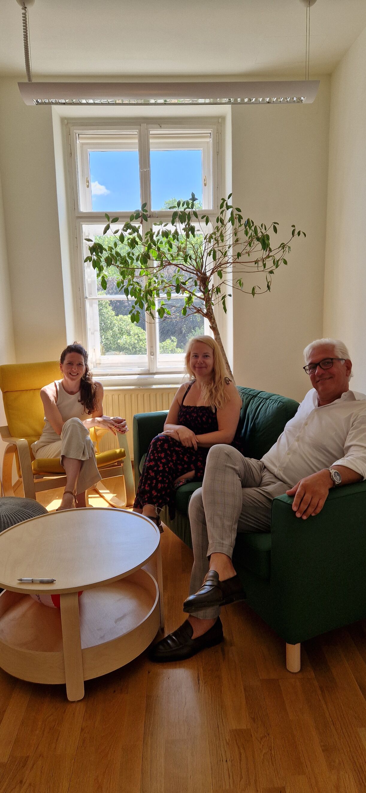 Drei Personen auf einen Couch sowie einem Wippstuhl.