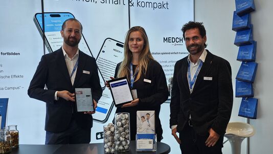 Zwei Männer und eine Frau stehend bei einem Messestand