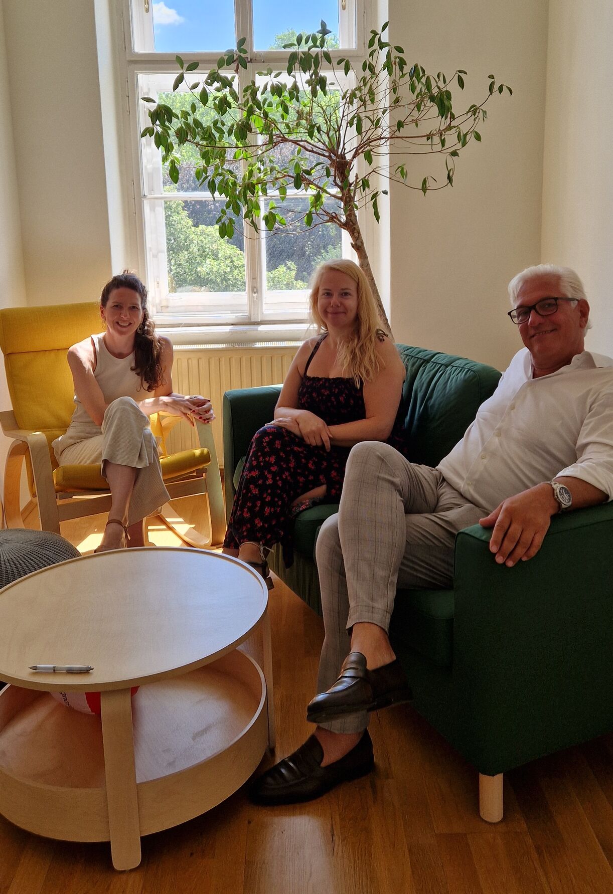 Drei Personen auf einen Couch sowie einem Wippstuhl.