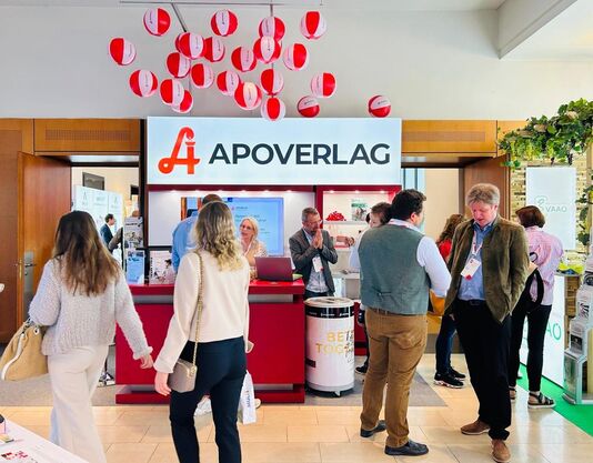 Nahaufnahme des APOVERLAG-Messestand beim APOkongress in Pörtschach 2024 mit den Besucherinnen und Besuchern. Es werden angeregte Gespräche geführt.