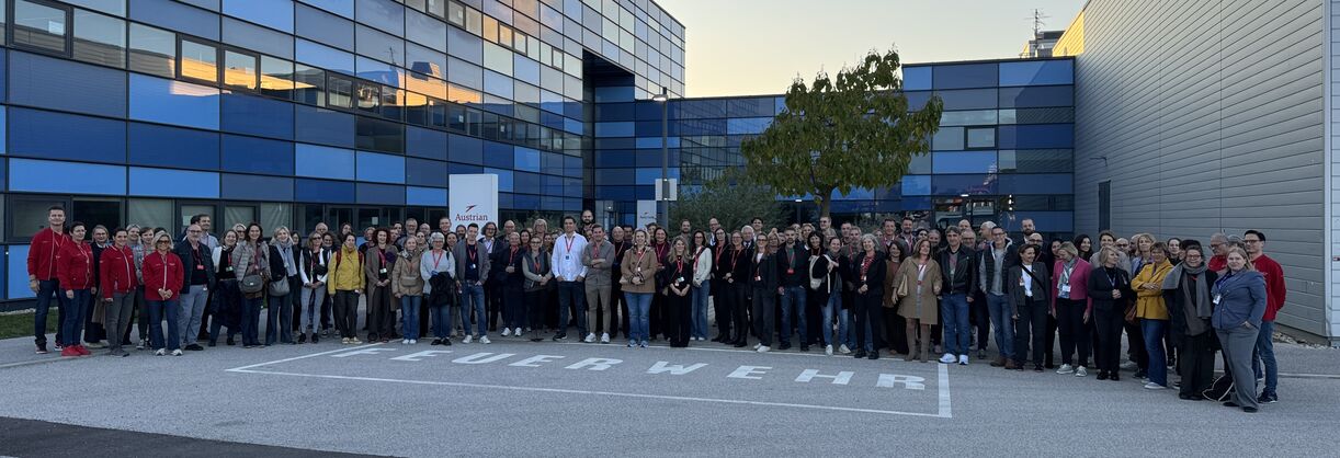 Personen stehen im Halbkreis zwischen Gebäudeteilen