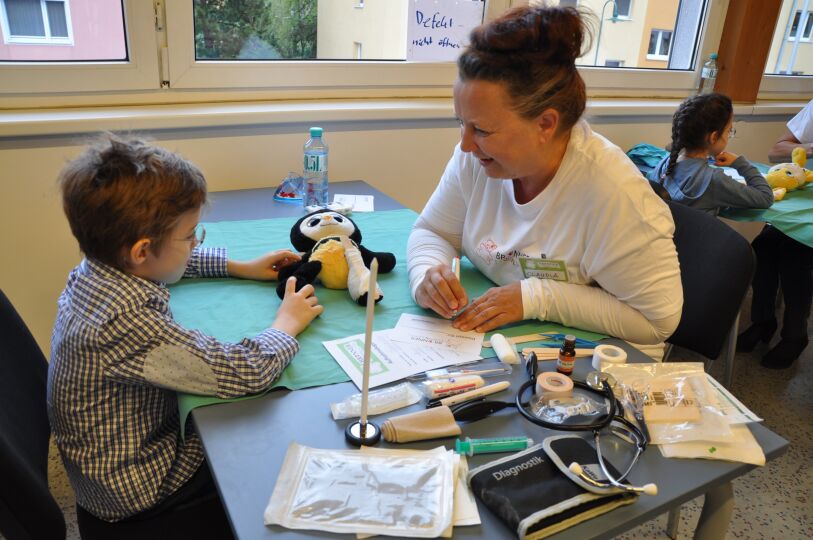 Brunner Teddyklinik Arztbesuch Brunner Teddyklinik Arztbesuch - Das Bild zeigt eine Betreuerin und ein Kind mit mitgebrachtem Stofftier, das die Brunner Teddyklinik besucht. Es soll ein Arztbesuch nachgestellt werden, um Kindern die Angst vor Arztbesuchen zu nehmen.