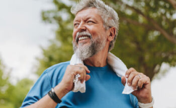 ÖAZtara Wissensquiz: Gesund älter werden - Ein älterer Mann sieht lächelnd zur Seite. Er hält sich an einem Handtuch in seinem Nacken fest.